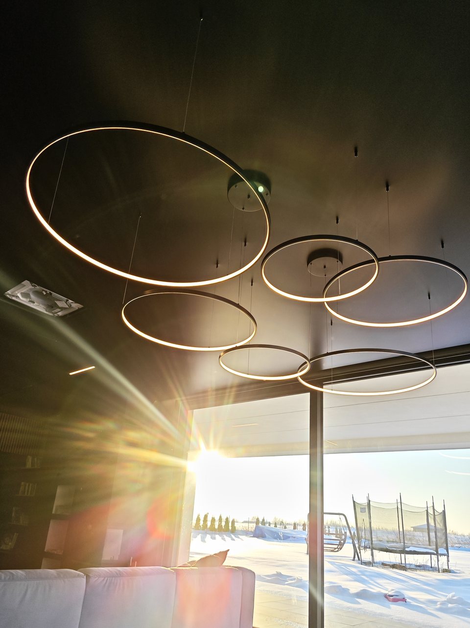 Lampy ring pod czarnym satynowym sufitem w słońcu wpadającym przez przeszklenia