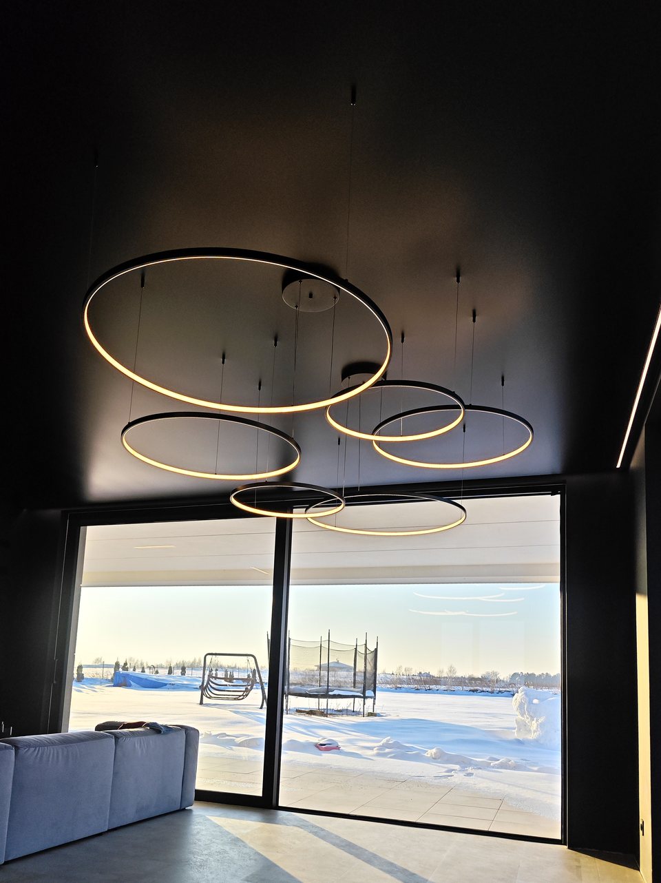 Pierścieniowe lampy LED na tle czarnego sufitu napinanego przy oknach tarasowych